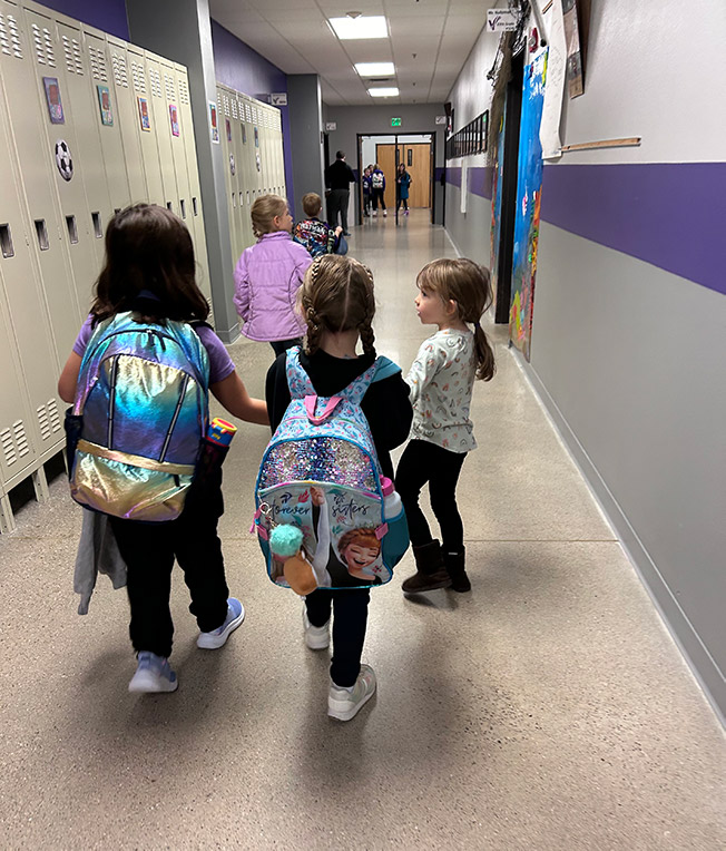 Young kids walking in a hallway wearing backpacks